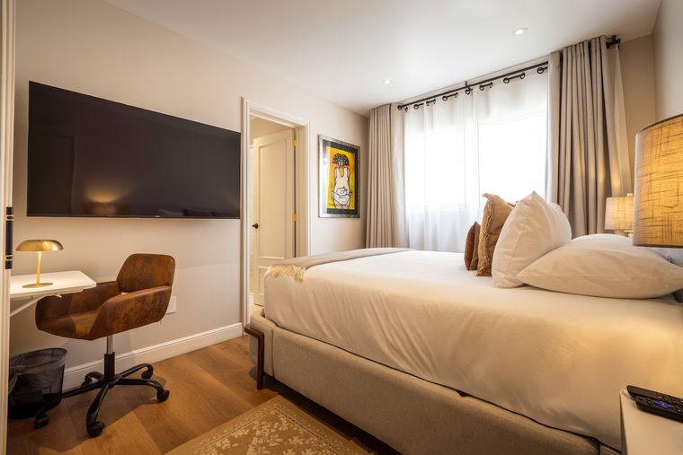 Cama queen con el escritorio y su silla al lado, y la televisión enfrente