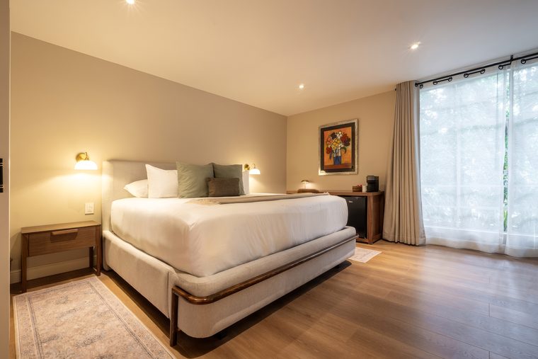 Cama king con ventanal y cortinas claras, y un cuadro sobre la cabecera