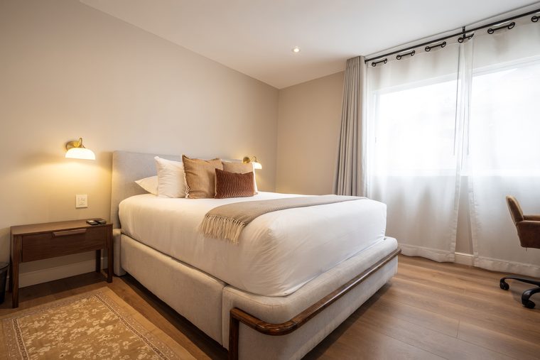 Cama queen con cortinas claras y lámparas de pared a los lados